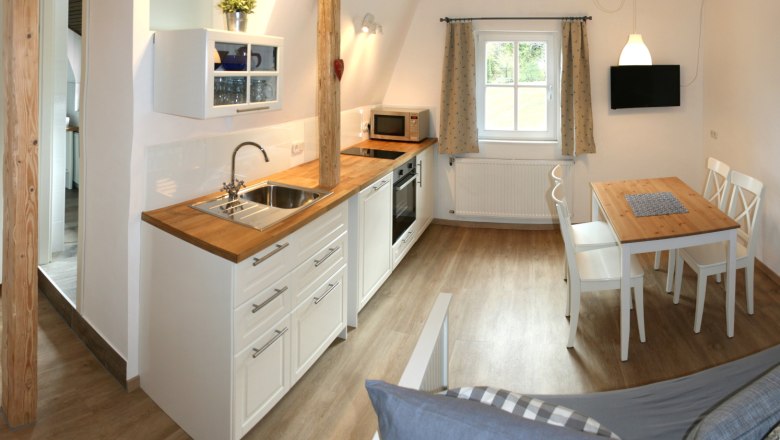 Apartment 1, © Marianne Gschaider Moderne Küche mit Holzboden, weißen Schränken, Esstisch und Fenster.