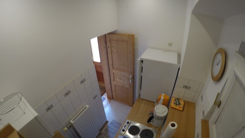 Küche Ferienwohnung 2, © dmgrauszer Kleine Küche mit Herd, Kühlschrank und Holztür.