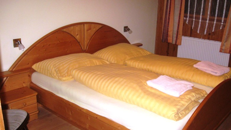 Zimmer, © Gruber Johann Holzbett mit gelber Bettwäsche in einem Zimmer.