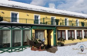 Gasthof Schmirl, © Bernhard Schmirl Gelbes Gebäude mit grünen Akzenten, beschriftet als Gasthof Schmirl, im Schnee.