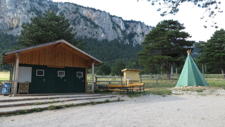 Zeltplatz Hohe Wand Blick Camp, © Naturpark Hohe Wand Ein Zeltplatz mit einem grünen Tipi, einer Holzhütte und Bänken vor einer Felswand und Bäumen.