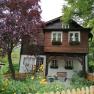 Landsitz Oberhof, © Wiener Alpen Ein zweistöckiges Holzhaus mit Blumenkästen und Garten.