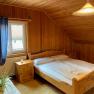 Doppelzimmer, © Wiener Alpen Gemütliches Doppelzimmer mit Holzverkleidung, Doppelbett, Fenster mit blauen Vorhängen und einer Pflanze auf dem Tisch.