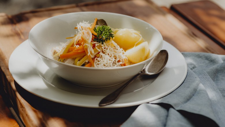 Krenfleisch vom Schweinsbauch, Wurzelstreifen, Salzerdäpfel, © Niederösterreich Werbung/Rita Newman Ein Teller mit Krenfleisch, Wurzelstreifen und Salzerdäpfeln, garniert mit Petersilie, auf einem Holztisch.