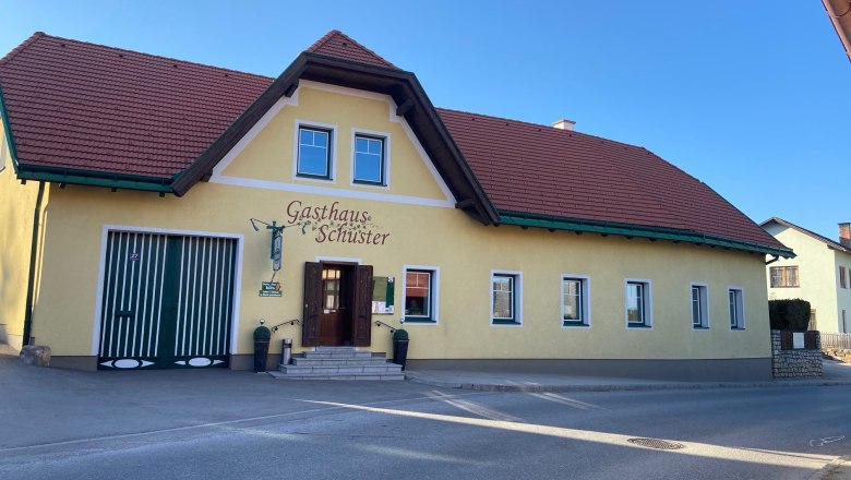 Gasthaus Schuster, © Wiener Alpen Gelbes Gebäude mit rotem Dach und der Aufschrift 'Gasthaus Schuster'.