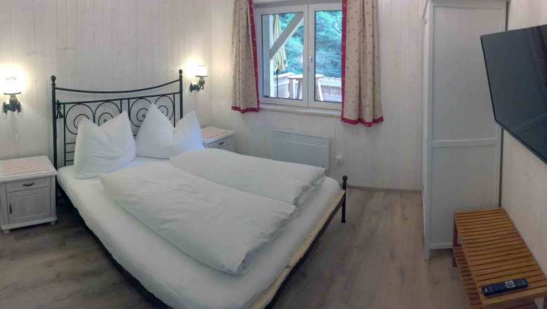 Ferienhaus, © Marianne Gschaider Schlafzimmer in einem Ferienhaus mit Doppelbett, TV und Fenster mit Vorhängen.