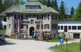 Alpin- und Heimatmuseum Hohe Wand, © Naturpark Hohe Wand Alpin- und Heimatmuseum Hohe Wand mit Besuchern und Fahnen vor dem Eingang.