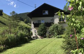 Außenansicht, © Familie Krenn Ein zweistöckiges Haus mit Balkon, umgeben von einem gepflegten Garten und grünen Hügeln im Hintergrund.