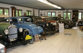 Oldtimermuseum Hausberger, © Leonhard Hausberger Innenansicht eines Oldtimermuseums mit mehreren klassischen Autos in einer Reihe.