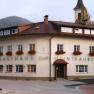 Hausansicht, © Gruber Johann Ein traditionelles Gasthaus mit Blumen an den Fenstern und einem Kirchturm im Hintergrund.