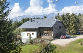 Öhler Schutzhütte, © Wiener Alpen, Franz Zwickl Eine Berghütte mit grauem Dach, umgeben von Bäumen und Bergen im Hintergrund.
