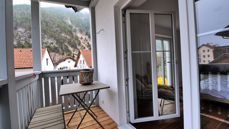 Balkon Top 4, © Daniela Sinadinoska Ein Balkon mit Tisch und Bank, umgeben von Bergen und Häusern mit roten Dächern.