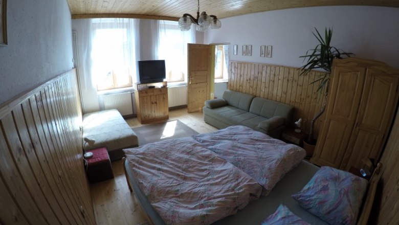 Schlafzimmer Ferienwohnung 1, © dmgrauszer Gemütliches Schlafzimmer mit Doppelbett, Sofa, TV und Holzmöbeln in einer Ferienwohnung.