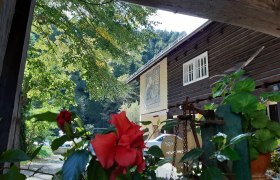 Idyllischer Hof, © Familie Kellner Ein traditionelles Holzhaus mit roten Blumen im Vordergrund und grünen Bäumen im Hintergrund.