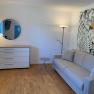 Wohnzimmer, © Marianne Gschaider Modernes Wohnzimmer mit grauem Sofa, Kommode, Spiegel und dekorativer Wandkunst.