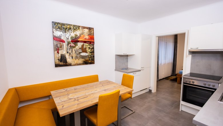 Küche, © Peter Prandstetter, Julian Eisenkirchner Moderne Küche mit gelber Eckbank, Holztisch und Kunstwerk an der Wand.