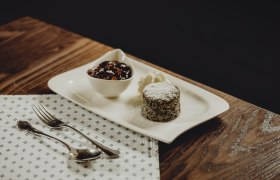 Dessert: Mohnkuchen, © Niederösterreich Werbung/Sophie Menegaldo Ein Mohnkuchen mit Puderzucker, Sahne und einer Schale mit Früchten auf einem weißen Teller.