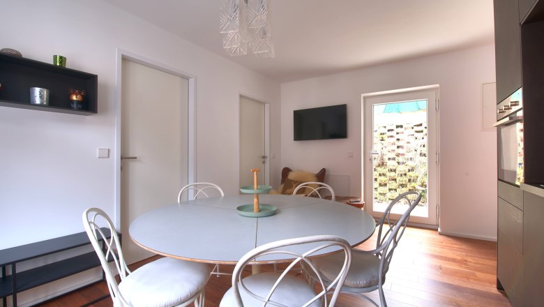 EssbereichTop 3, © Daniela Sinadinoska Moderner Essbereich mit rundem Tisch, weißen Stühlen und hölzernem Boden.