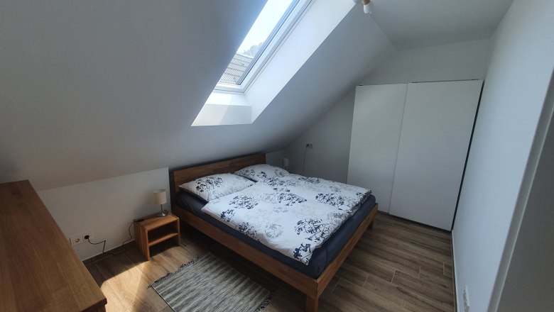 Schlafzimmer - Ferienwohnung Stampfbauer, © Tobias Micke Modernes Schlafzimmer mit Dachfenster, Doppelbett, Holzmöbeln und weißem Kleiderschrank.