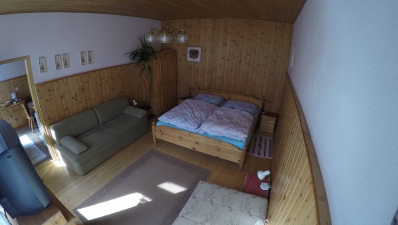 Schlafzimmer Ferienwohnung 1, © dmgrauszer Ein gemütliches Schlafzimmer mit Holzwänden, einem Doppelbett, einem Sofa und einem Teppich auf Holzboden.