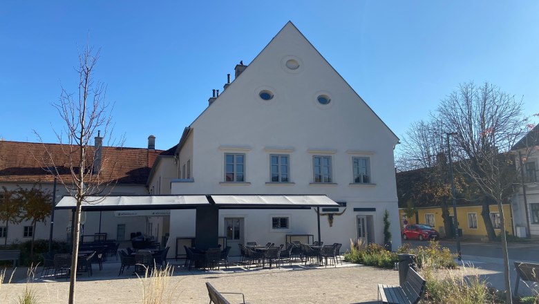 Gastgarten - Zum Riegler, © Wiener Alpen Ein Gastgarten mit leeren Tischen und Stühlen vor einem weißen Gebäude mit spitzem Dach an einem sonnigen Tag.