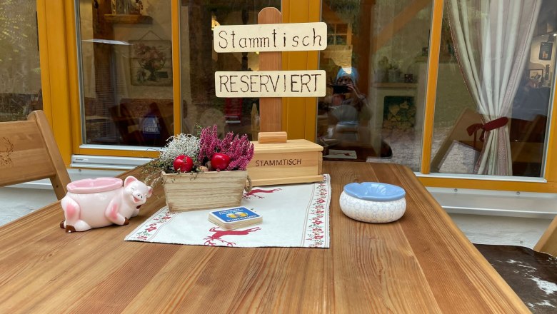 Stammtisch, © KlammWirtin Ein rustikaler Tisch mit einem Schild 'Stammtisch Reserviert', Dekorationen und einem Aschenbecher.