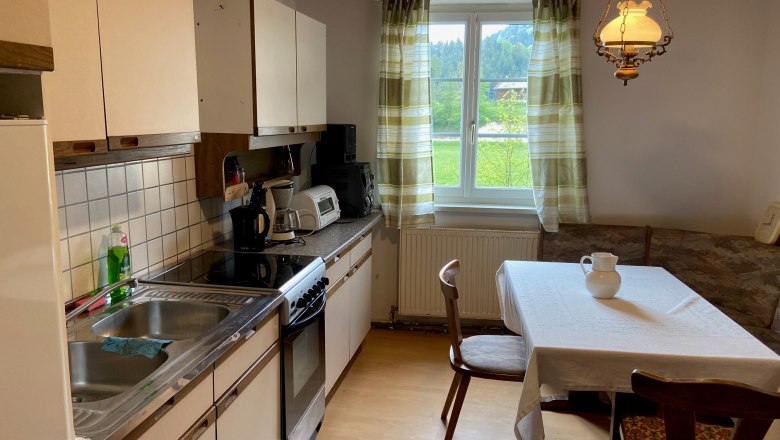 Küche, © Wiener Alpen Küche mit Esstisch, Stühlen, Spüle, Herd und Fenster mit Vorhängen.