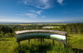 Blickplatz Blumberg, © Wiener Alpen, Christian Kremsl Panoramablick von einem Aussichtspunkt mit Infotafel, im Hintergrund eine weite Landschaft und blauer Himmel.