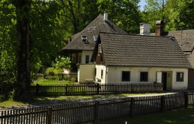 Gästehaus, © fritz fischer Ein traditionelles Gästehaus mit Holzzaun und Garten, umgeben von Bäumen.