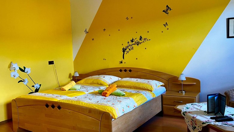 Frühstückspension Csenar, © Christine Kreiderits Gemütliches Schlafzimmer mit gelber Wand, Doppelbett und dekorativen Schmetterlingen an der Wand.
