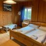 Doppelzimmer, © Wiener Alpen Holzvertäfeltes Doppelzimmer mit Bett, Tisch, Stuhl und Fenster.