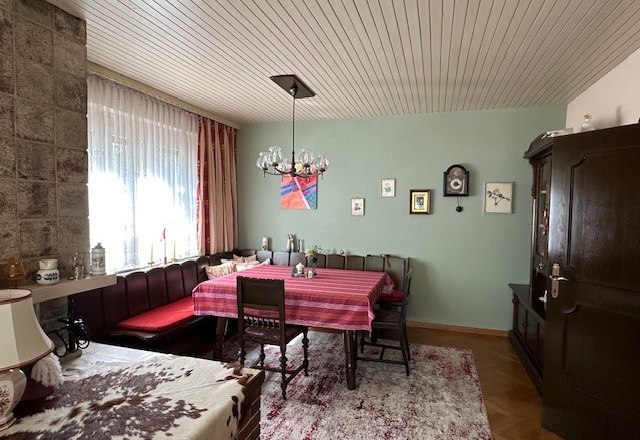 Gemütliches Wohnzimmer mit Esstisch, Eckbank, Teppich und Wanduhr.