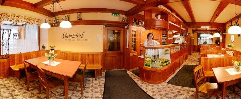 Panorama einer gemütlichen Gaststube mit Holzmöbeln und dekorativen Lampen.