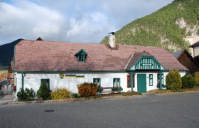 Schneebergmuseum Puchberg, ein traditionelles Gebäude mit grünem Dach und Schornstein, umgeben von Bergen und Bäumen.