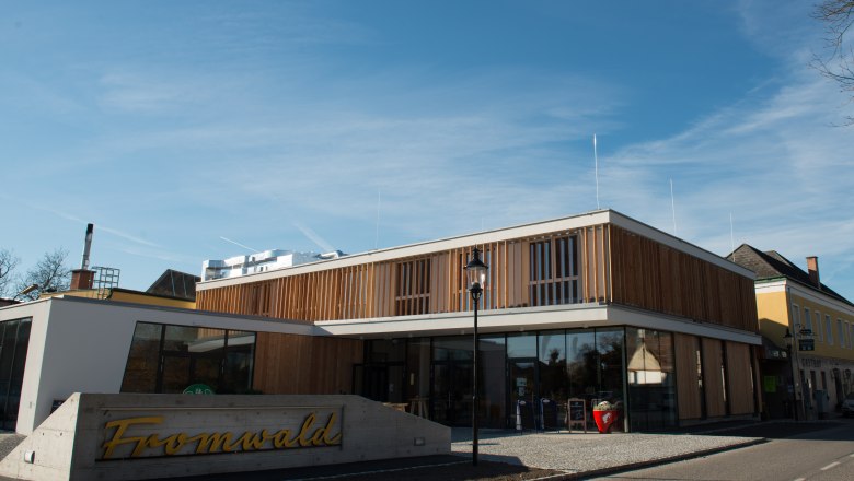 Modernes Gebäude mit Holzfassade und Glasfront, davor ein Schild mit der Aufschrift 'Fromwald'.