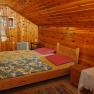 Holzvertäfeltes Schlafzimmer mit Doppelbett, bunten Decken und offenem Fenster.