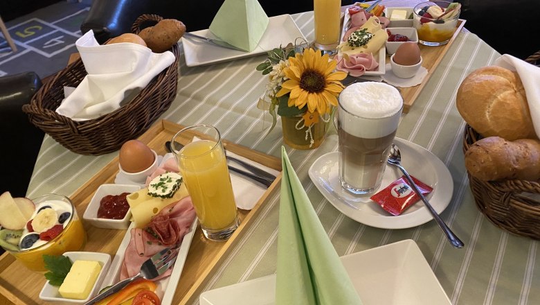 Ein gedeckter Frühstückstisch mit Brötchen, Aufschnitt, Eiern, Saft und Kaffee in einer Pension.