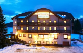 Beleuchtetes Gebäude der Pension Bruckerhof im Schnee bei Dämmerung.
