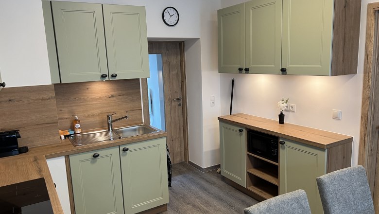 Moderne Küche mit grünen Schränken, Holzarbeitsplatten und grauen Stühlen.