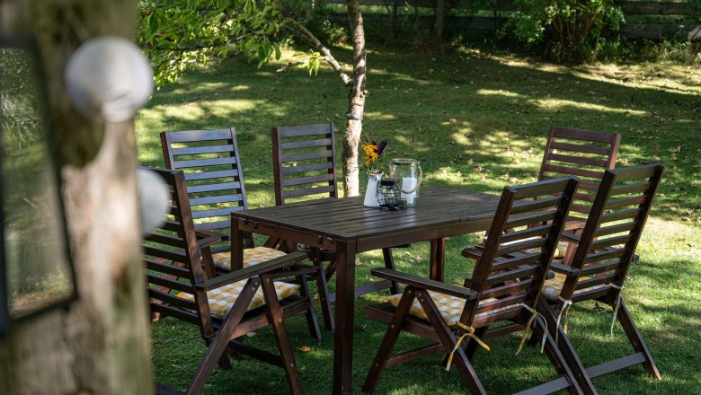 Garten mit Holztisch und St&uuml;hlen, dekoriert mit Blumen und Kerzen.