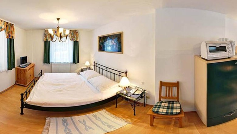 Kleines Schlafzimmer mit Doppelbett, Nachttischen, TV, Mikrowelle und Stuhl.