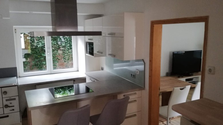 Moderne Küche mit Kochinsel, weißen Schränken und Fenster mit Blick ins Grüne.