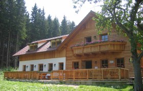 Eine rustikale Berghütte aus Holz mit Balkon und Terrasse, umgeben von Bäumen.