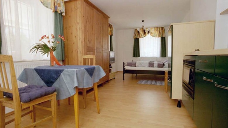 Kleine Wohnung mit Holzm&ouml;beln, Esstisch, St&uuml;hlen, Bett und K&uuml;chenzeile.