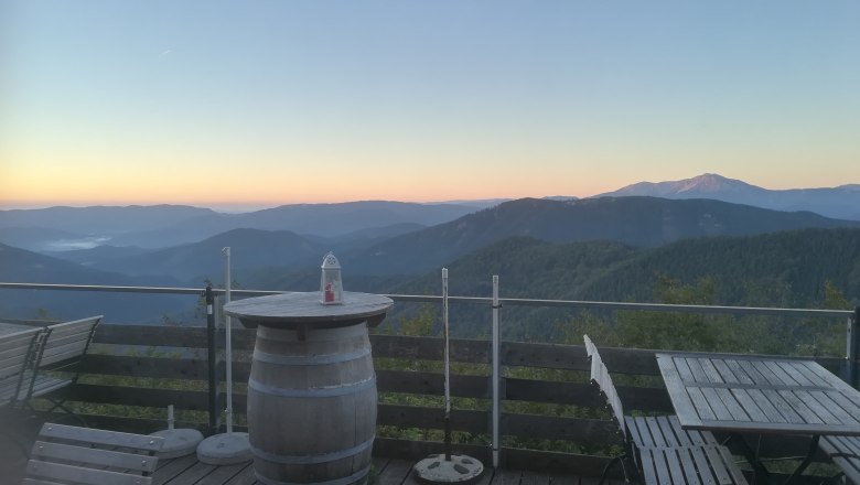 Terrasse mit Holzmöbeln und Bergblick bei Sonnenaufgang.