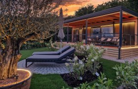 Ein modernes Chalet mit Terrasse und Liegestühlen im Garten bei Sonnenuntergang.