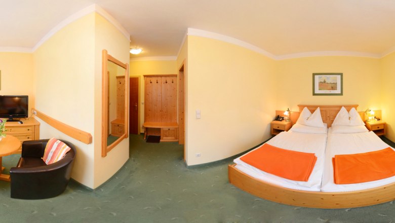 Panorama eines Hotelzimmers mit Doppelbett, Tisch, zwei Sesseln und Fernseher.
