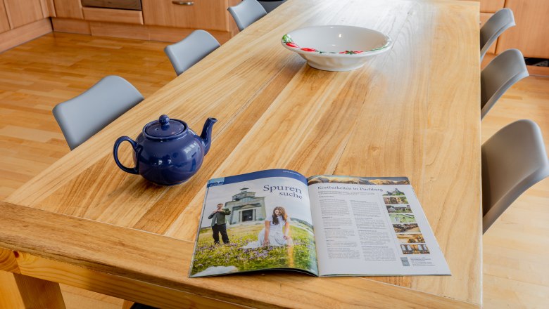 Ein Holztisch mit einer blauen Teekanne, einer Sch&uuml;ssel und einer Zeitschrift in einer K&uuml;che.