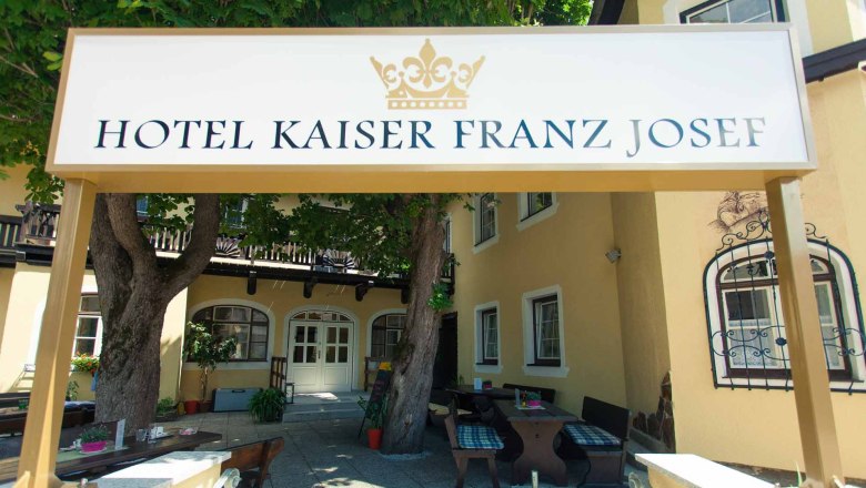 Eingang des Hotel Kaiser Franz Josef mit Schild und Bäumen.