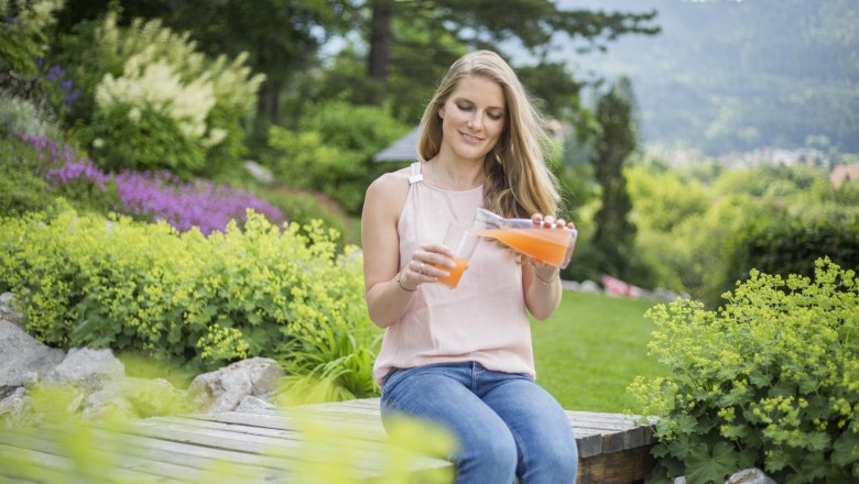 Frau sitzt im Garten und gießt Saft in ein Glas.